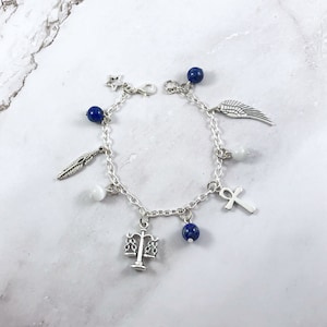 May include: A silver charm bracelet with blue and white beads, and charms including a feather, a star, a wing, a scale, an ankh, and a white stone.