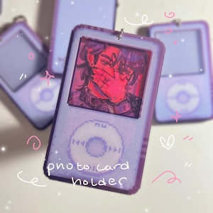 Puede incluir: Un portatarjetas fotográfico lila con un diseño pixelado que se asemeja a un reproductor de música. El soporte presenta un retrato con tonos rojos y rosas. El texto "photo card holder" es visible en la parte delantera.