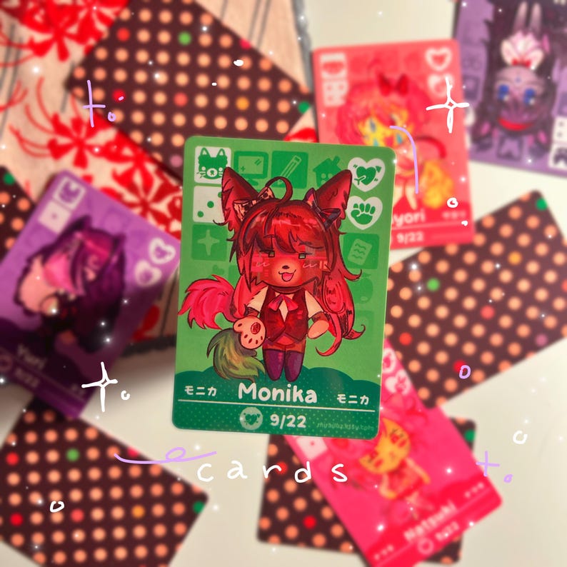 Puede incluir: Una tarjeta coleccionable rectangular con fondo verde que presenta un personaje estilizado de pelo rojo con orejas y cola de animal. La tarjeta muestra el nombre Monika en texto blanco, la fecha 9/22 y varios iconos peque&ntilde;os, incluyendo un coraz&oacute;n.