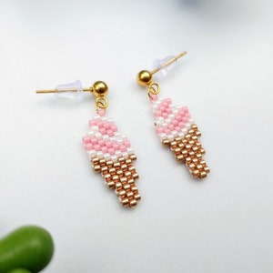 May include: A pair of gold tone earrings with pink and white beaded ice cream cone designs.