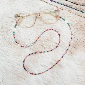 May include: A colourful beaded glasses chain with small white and coloured charms. The chain is looped around a pair of clear glasses with a brown frame.