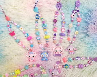 May include: A set of six colorful phone charms featuring various cartoon characters, including Stitch, a green monster, and a pink pig. The charms are made of beads and feature a variety of colors, including pink, purple, blue, green, and yellow.