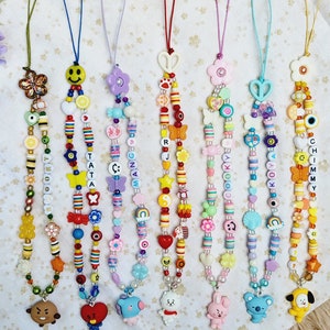 May include: Seven colourful beaded phone charms with different character charms at the bottom. The charms are in the shape of a bear, a heart, a blue bird, a white bunny, a koala, and a yellow puppy. The beads are in various colours, including red, yellow, blue, green, and pink. The charms are all strung on a thin string.
