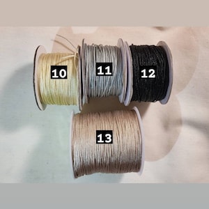 May include: Four spools of thread in different colours: beige, light grey, black, and a darker grey. The spools are labelled with numbers 10, 11, 12, and 13.