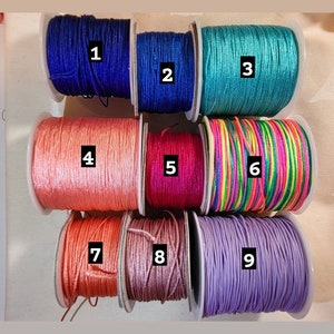 May include: Nine spools of colourful embroidery floss, numbered 1 through 9. The floss colours are blue, teal, peach, pink, rainbow, lavender, coral, and light pink.