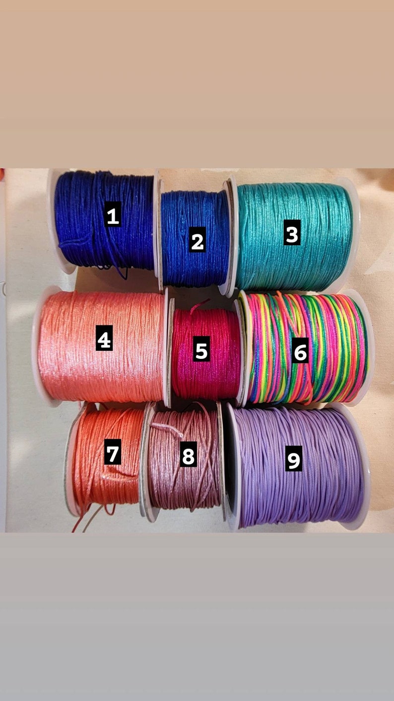 May include: Nine spools of colourful embroidery floss, numbered 1 through 9. The floss colours are blue, teal, peach, pink, rainbow, lavender, coral, and light pink.