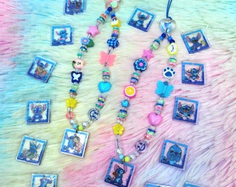 May include: Two blue and white phone charms with colorful beads and charms, including butterflies, hearts, stars, and flowers. The charms feature a cartoon character with blue fur and large ears.