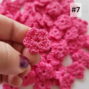 May include: A collection of small, five-petaled hot pink crochet flowers. Each individual flower is crafted from yarn with a central circular detail. A white square label with the black text #7 is visible in the upper right corner of the image.
