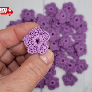 May include: A collection of small, crocheted purple flowers. The flowers are about 1 inch in diameter and have a five-petal design.