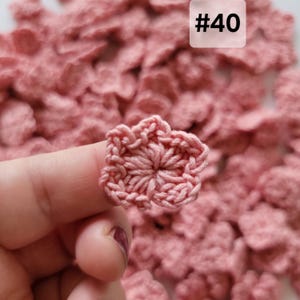 May include: A small, dusty pink crocheted flower applique with five rounded petals and a textured center. The item is labeled with the text #40. The flower is crafted from yarn and features a repeating stitch pattern throughout the design.