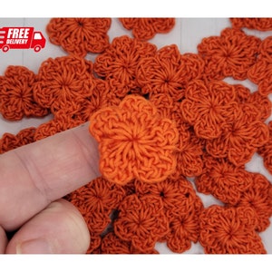 May include: A pile of orange crocheted flowers. The flowers are small and have a five-pointed star shape.