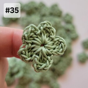 May include: A sage green crochet flower applique with five rounded petals and a central hole. The item is labeled with the text #35 in the upper left corner. The crochet work features a visible yarn texture and a consistent light green color.
