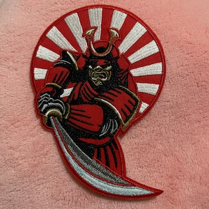 May include: Red and white embroidered patch of a samurai warrior holding a sword in front of a rising sun design.
