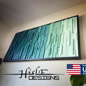 May include: A teal and green wood wall art piece with a black frame. The art is made up of vertical wooden slats of varying lengths and widths. The art is titled "Hisle Designs" and has a "Made in USA by Hand" label in the bottom right corner.