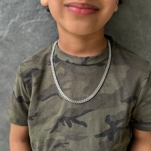 May include: A silver curb chain necklace on a person wearing a camouflage shirt.