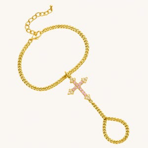 May include: Gold-toned hand chain bracelet featuring a cross pendant. The cross is adorned with pink and clear gemstones. The bracelet has a curb chain design and a ring that fits over the finger.