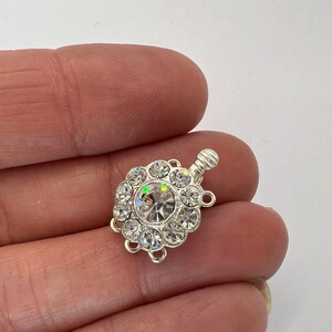 May include: Silver-toned clasp with a round crystal center surrounded by smaller crystals. The clasp has three loops for attaching to jewelry.