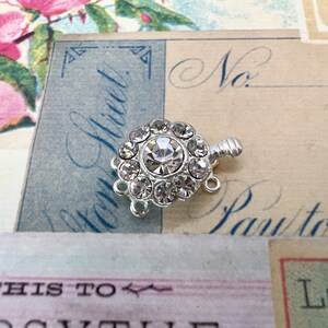 May include: Silver tone clasp with a clear rhinestone center surrounded by smaller rhinestones. The clasp has three loops for attaching to a necklace or bracelet.
