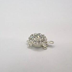 May include: Silver-toned clasp with a round design featuring clear rhinestones. The clasp has three loops for attaching jewelry.