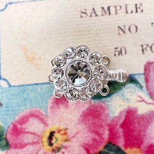 May include: Silver-toned clasp with a large clear rhinestone surrounded by smaller rhinestones. The clasp has three loops for attaching to a necklace or bracelet.