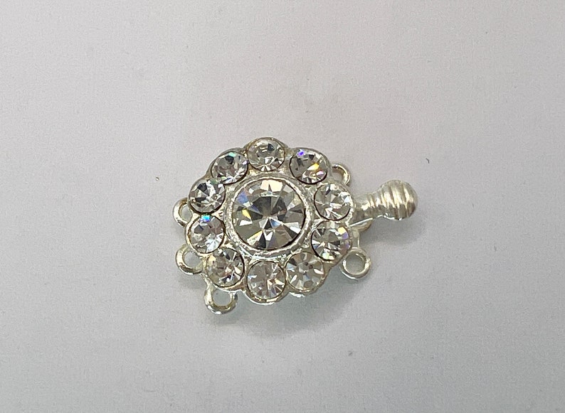 May include: Silver tone clasp with a large clear rhinestone in the center surrounded by smaller clear rhinestones.