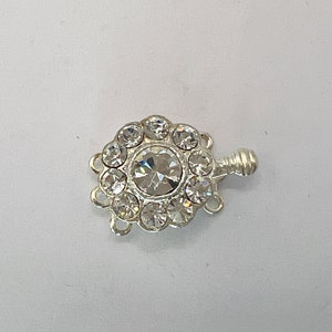 May include: Silver-toned clasp with a clear crystal center surrounded by smaller clear crystals. The clasp has three loops for attaching jewelry.