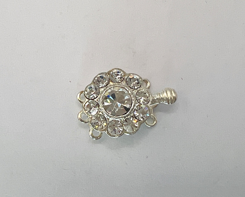 May include: Silver-toned clasp with a clear crystal center surrounded by smaller clear crystals. The clasp has three loops for attaching jewelry.