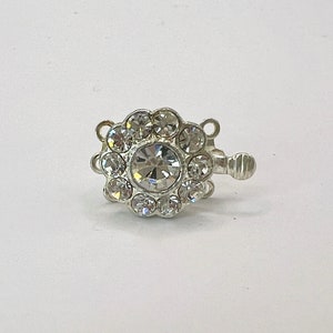May include: Silver-toned clasp with a large clear rhinestone surrounded by smaller rhinestones. The clasp has three loops for attaching jewelry.