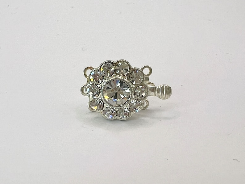 May include: Silver-toned clasp with a large clear rhinestone surrounded by smaller rhinestones. The clasp has three loops for attaching jewelry.
