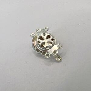 May include: Silver-toned metal clasp with five loops for attaching jewelry or other items. The clasp has a decorative design with a cross-shaped cutout.