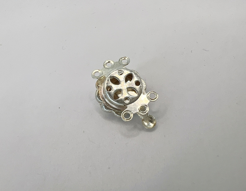 May include: Silver-toned metal clasp with five loops for attaching jewelry or other items. The clasp has a decorative design with a cross-shaped cutout.