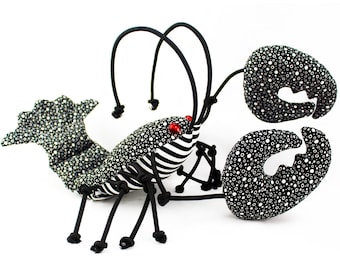 May include: A black and white striped lobster with red eyes and black legs. The lobster is made of fabric and has a textured surface.