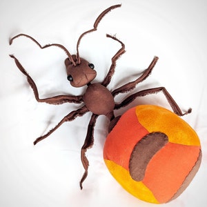 May include: A brown plush ant with long legs and a large, round, orange and brown abdomen. The ant is lying on its back with its legs spread out.