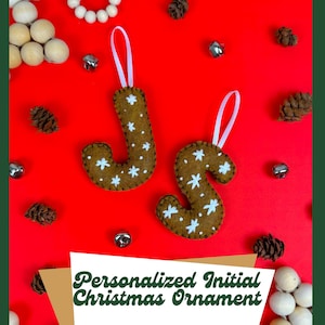 May include: Two felt Christmas ornaments shaped like the letters J and S. The ornaments are brown with white snowflake designs and are hanging from white ribbon.