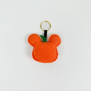 May include: A felt pumpkin keychain with a green stem and a gold key ring. The pumpkin is orange and has a stitched design.