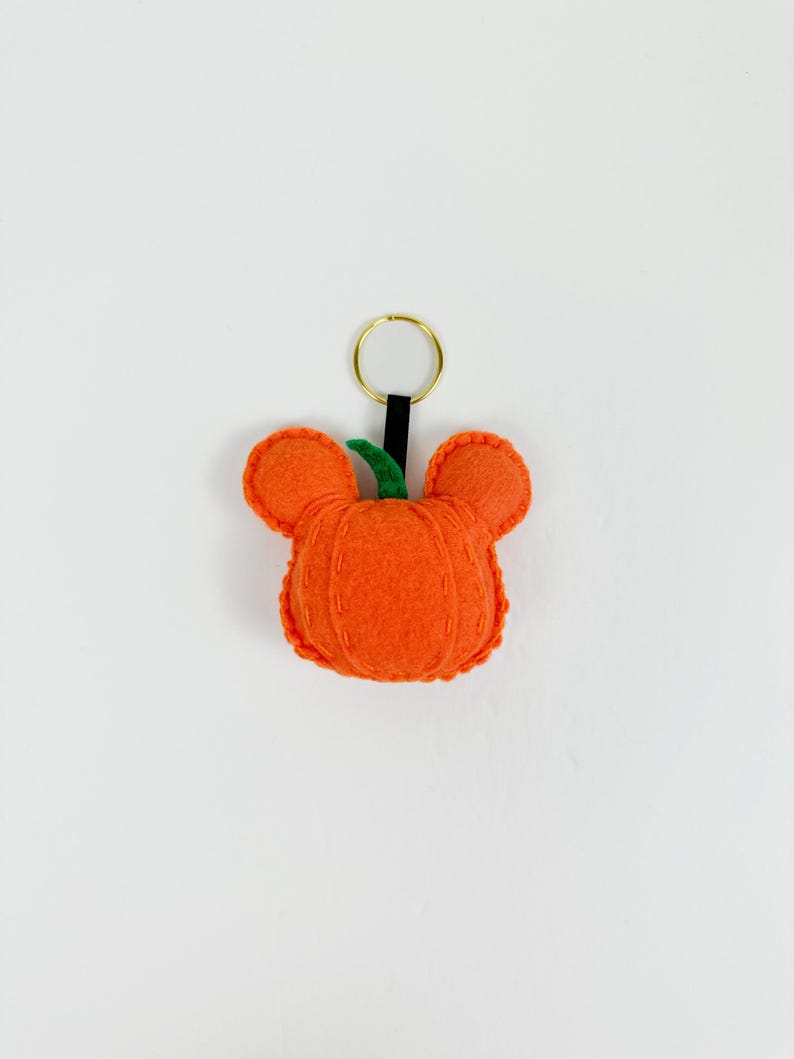 May include: A felt pumpkin keychain with a green stem and a gold key ring. The pumpkin is orange and has a stitched design.