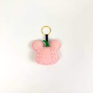 May include: A pink felt pumpkin keychain with a green stem and a black and gold key ring.