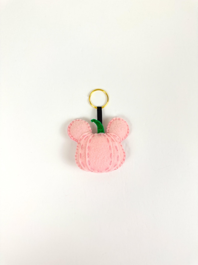 May include: A pink felt pumpkin keychain with a green stem and a black and gold key ring.