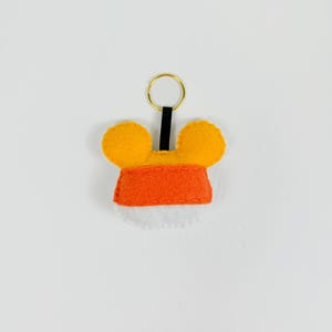 May include: A felt keychain with orange and yellow ears and a red felt body. The keychain has a gold metal ring.