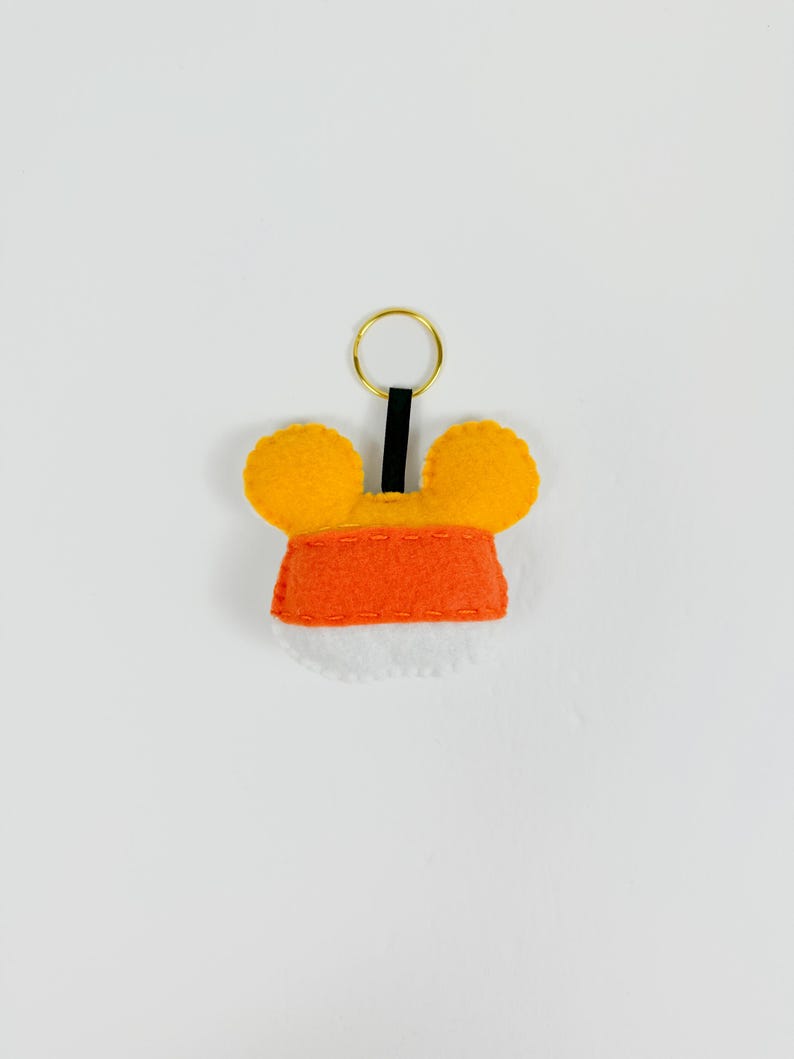 May include: A felt keychain with orange and yellow ears and a red felt body. The keychain has a gold metal ring.