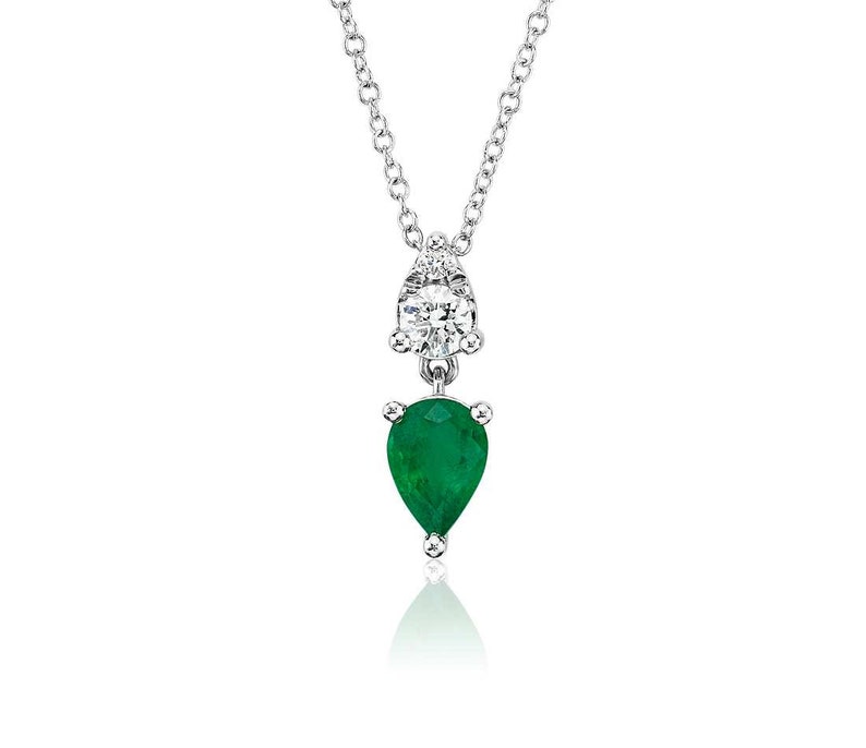 May include: A silver necklace with a pear-shaped emerald pendant and a round diamond accent. The emerald is a vibrant green color, and the diamond sparkles. The necklace hangs from a delicate chain, creating an elegant look.