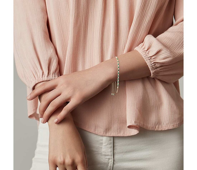 May include: A delicate silver bracelet with a row of small green gemstones. The bracelet has a sliding clasp for adjustability.