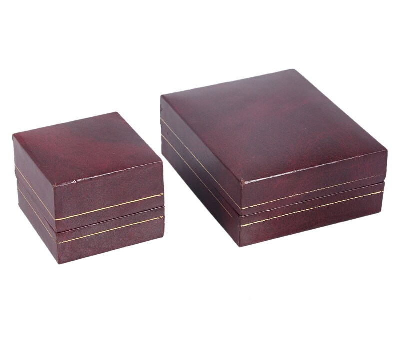 May include: Two burgundy-colored gift boxes with gold trim. The larger box is on the right and the smaller box is on the left.