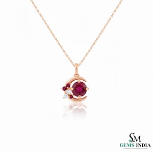 Puede incluir: Collar de oro rosa con colgante de media luna. El colgante presenta una gema roja oscura grande y redonda, gemas rojas más pequeñas y piedras blancas. La cadena es delicada y el diseño es elegante.