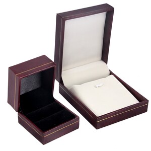 May include: Two burgundy jewelry boxes with gold trim. The larger box is open and has a white velvet interior. The smaller box is closed and has a black velvet interior.