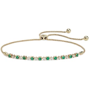May include: A gold chain bracelet with a sliding clasp. The bracelet is adorned with a row of emerald green and clear round gemstones.