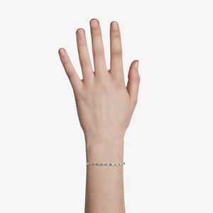 May include: A gold bracelet with green gemstones. The bracelet is on a person's wrist.