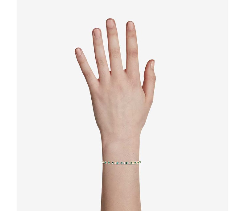 May include: A gold bracelet with green gemstones. The bracelet is on a person's wrist.