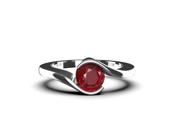 May include: A silver ring featuring a large, round, deep red gemstone. The band curves around the gemstone, creating a modern design. The ring is set against a white background, highlighting its polished finish.