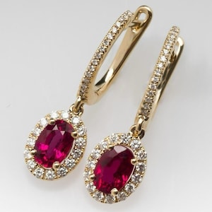 May include: A pair of gold drop earrings with oval ruby gemstones, each encircled by small diamonds. The earring hooks are also set with small diamonds, creating a sparkling and elegant design.